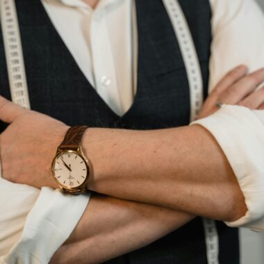 A tailor crosses arms showing a stylish wristwatch and tape measure, representing precision craftsmanship.
