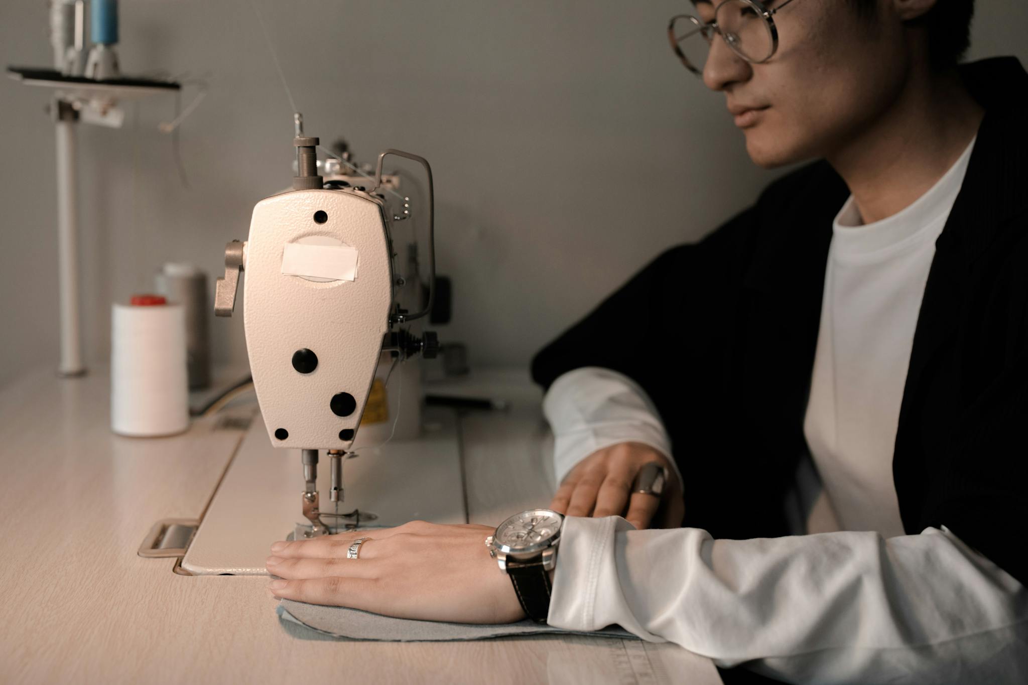 Asian man tailor attentively sewing fabric with a machine in a studio.