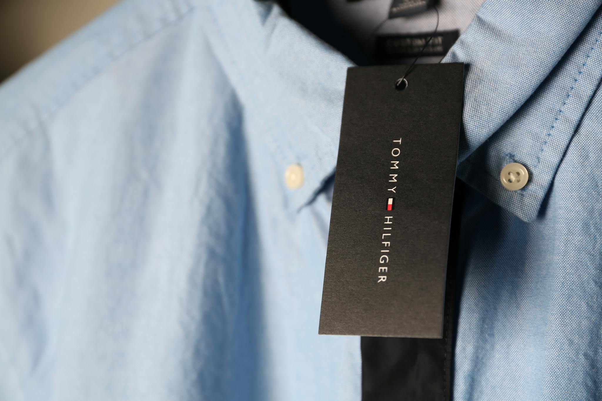 Detailed close-up of a blue dress shirt featuring a black tag with branding.