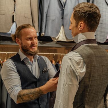 Tailor assists customer in clothing store with suit fitting. Professional attire and tailoring service.