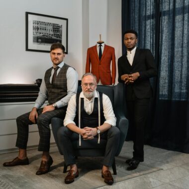 Three male fashion designers in a tailoring studio showcasing elegant suits and craftsmanship.